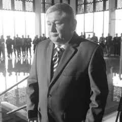 Jan Harhaj, starosta lidzbarski, w garniturze, stoi przed grupą ludzi w jasnym pomieszczeniu.