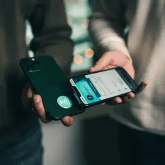 Dwie osoby trzymają iPhone'y. Jeden telefon zbliża się do drugiego, aktywując funkcję NFC.