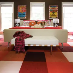 A dog lounges on a bed in a room with a bold, kitsch style. The floor features a checkered pattern of red and brown squares, and the walls are adorned with Campbell's soup can art.