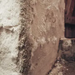 Strukturierte Wand mit salpeter tapete, die an einer Ecke abblättert und eine raue, kristalline Textur offenbart.
