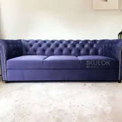 Elegancka, granatowa kanapa chesterfield z pikowanego welwetu, ozdobiona srebrnymi pineskami.