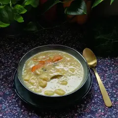 Aromaticzna zupa na żeberkach z kawałkami marchewki i ziemniaków, podana w misce obok złotej łyżki.
