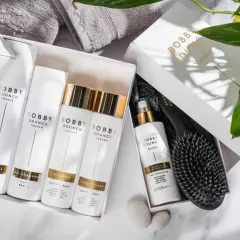 En presentbox med Bobby Oduncu-produkter för att ta hand om håret: hårspray, torrschampo, schampo, balsam och leave-in spray. En borste ligger bredvid.