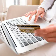 Kobieta z kartą płatniczą wpisuje kod BIC na laptopie, realizując płatność online.