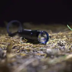 Latarka Olight M2R Warrior leży na ściółce leśnej, gotowa do akcji.
