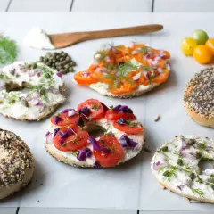 Flera bröd med hål i mitten, toppade med färskost, lax, tomater, rödlök och dill. Ett härligt urval av bagels!