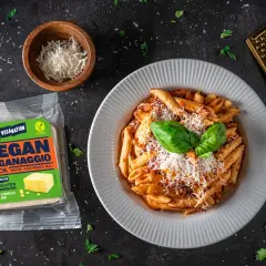 Talerz penne z sosem, opakowanie wegańskiego parmezanu i złota tarka.