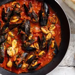Cozze alla tarantina in padella, un piatto succulento con pane fresco a lato.