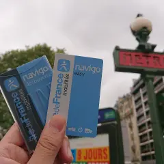 Dłoń trzyma karty Navigo na tle paryskiego metra.