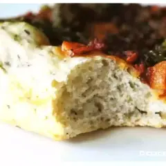 Gros plan sur une tranche de pâte à pizza sans gluten moelleuse, garnie de tomates et d'herbes.