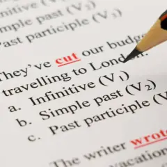 Matita evidenzia "cut" e "wrote" su un foglio con esercizi di grammatica inglese, tra cui la forma infinito.