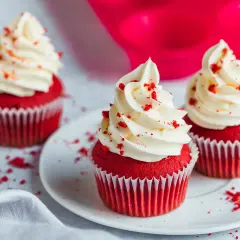 Drei rote Samt-Cupcakes mit cremiger weißer Glasur und roten Krümeln.