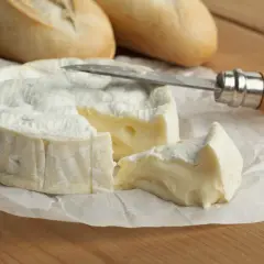 Queso camembert como se come: un trozo cremoso y un cuchillo listo para untar sobre pan.