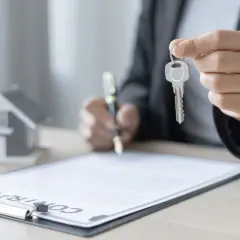 Persona firma un contrato de alquiler con opción a compra, sosteniendo la llave de una casa en miniatura.
