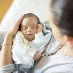 Śpiący noworodek w ramionach mamy. Czas z maleństwem jest bezcenny, a pytanie "noworodek do kiedy" szybko staje się nieistotne.
