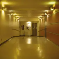 Korytarz z żółtym, błyszczącym podłogą i rzędem lamp. Oświetlenie awaryjne zapewnia bezpieczeństwo.