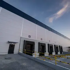 Nowoczesne centrum logistyczne InPost z rampami załadunkowymi i drzwiami, pod błękitnym niebem.