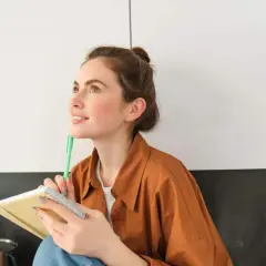 Ragazza pensosa, con un quaderno e una penna, dallo sguardo sognante. Una persona curiosa e operosa.