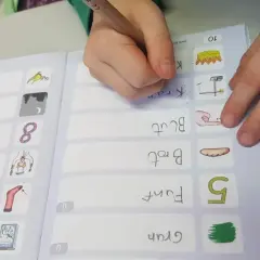 Kind schreibt im Rahmen des Förderunterrichts Grundschule Wörter wie "Kran" und "Brot" in ein Übungsheft.
