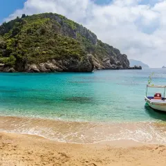 Piękna plaża na Korfu, turkusowa woda, łódka i tawerny. Ceny wakacji na Korfu mogą być różne, ale widok wart jest każdej złotówki.