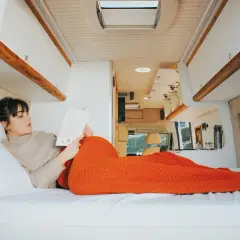 Une femme lit un livre, confortablement installée dans son camping-car fraîchement rénové. L'espace est lumineux et moderne.