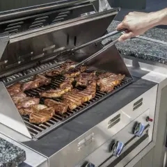 Un homme utilise une pince pour retourner des côtes levées sur un gril à gaz. L'odeur alléchante de la viande cuite emplit l'air.
