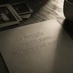 Vecchie foto di famiglia, una tazza e una penna su un tavolo. La frase "La famiglia forma chi siamo, nel bene e nel male" evoca ricordi, anche quando i figli ti feriscono.