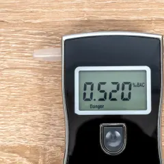Alkomat z wyświetlaczem pokazującym 0.520 %BAC i napisem "Danger" na drewnianym tle.