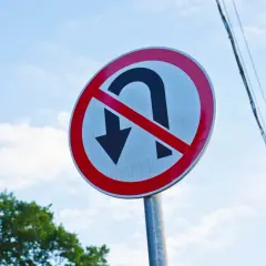 Znak zakazu zawracania na skrzyżowaniu. Nie można tu zawracać, więc lepiej jechać prosto lub skręcić.