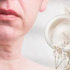 Un vasetto di crema e fiori secchi accanto al viso di una donna, suggerendo come migliorare la pelle del viso con prodotti naturali.