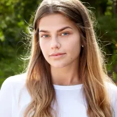 En ung kvinna med blont hår och blå ögon, en blivande top model Sverige, ler mot kameran utomhus.
