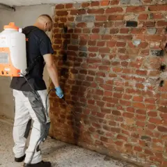 Mann mit Sprühgerät dichtet Kellerwand von innen ab.