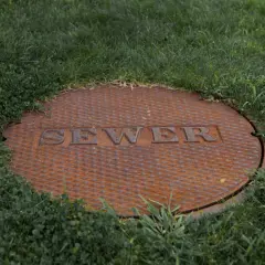 Zardzewiała pokrywa szamba z napisem "SEWER" w trawie. Czy na szambo trzeba mieć pozwolenie?