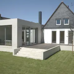 Nowoczesna dobudówka z betonu i szkła harmonijnie łączy się ze starym domem, tworząc przestronny taras i ogród.