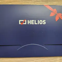 Chcesz wiedzieć, ile kosztuje voucher do kina Helios? Na zdjęciu widać elegancką, granatową kopertę z logo Helios i czerwoną wstążką, idealną na prezent.