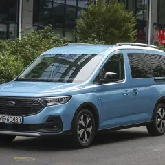 Błękitny ford 7 osobowy na tle nowoczesnego budynku. Idealny dla rodziny na wakacyjne wyprawy.