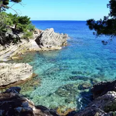 Agua cristalina en una cala rocosa, con escaleras de piedra que bajan al mar. El sol ilumina el fondo marino, creando un espectáculo de luz y color.