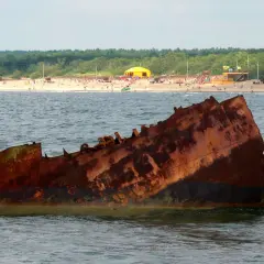 Rdza rdzy, wrak statku na Bałtyku. Czy to symbol, dlaczego wody bałtyku są znacznie zanieczyszczone? W tle plaża z ludźmi.