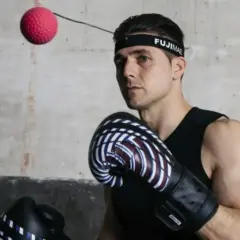 Bokser w rękawicach i opasce FUJIMAE, japoński producent sprzętu sportowego, ćwiczy z piłką refleksyjną.