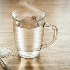 Łyżka soli i szklanka ciepłej wody, gotowe do płukania gardła solą.