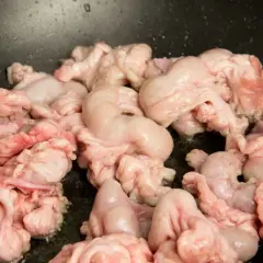 Unos gallinejas y entresijos crudos se cocinan en una sartén negra, listos para ser un plato tradicional.