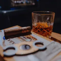 Un verre de whisky ambré et un cigare posés sur une boîte de cigares, prêts pour un moment de détente.
