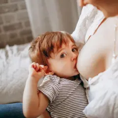 Un bimbo con occhi grandi e curiosi viene allattato dalla mamma. Un momento intimo, un gesto naturale, un esempio di allattare in pubblico senza timori.