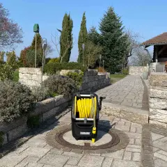 Ein gelber Schlauchwagen steht auf einem gepflasterten Weg im Garten, bereit für die Gartenarbeit.