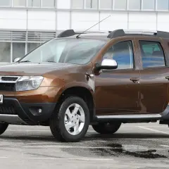 Brązowy Dacia Duster na parkingu, gotowy do testu. Widoczny kierowca za kierownicą.