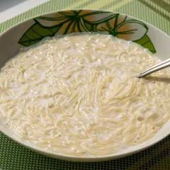 Zupa mleczna z makaronem, podana w misce z motywem kwiatowym, na zielonej podkładce.