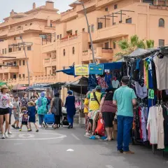 Gente comprando ropa en puestos del paseo marítimo de Garrucha. Edificios naranjas al fondo.