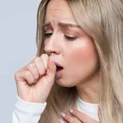 Mujer rubia con expresión de malestar, tosiendo y sujetándose el pecho. Sufre dolor en el pecho al toser sin fiebre.