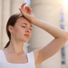 Une jeune femme essuie sa sueur sous un soleil de plomb, se demandant combien de temps dure un coup de chaleur.
