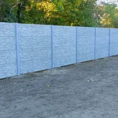 Mężczyzna z łopatą przy betonowym ogrodzeniu, zastanawia się, jak podwyższyć ogrodzenie betonowe, by zyskać więcej prywatności.